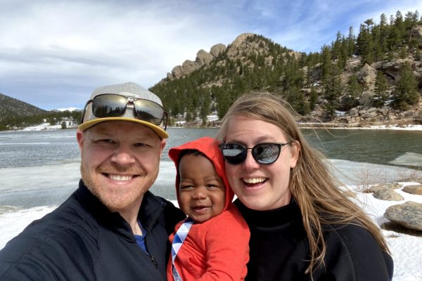 family smiling in front of lake and mountains